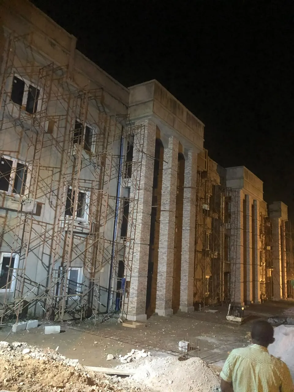 Stone-clad pilasters on a large building under scaffolding, lit at night