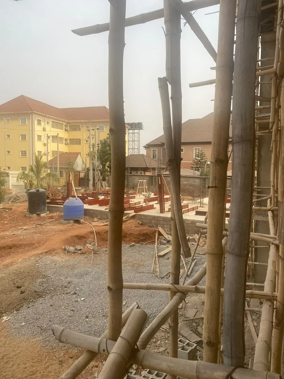 Steel frame members set out on a ground-floor slab, seen through scaffolding